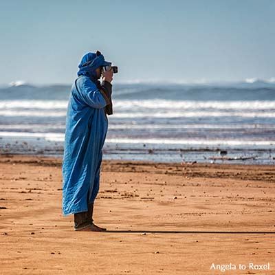 Fotograf in blauer Kleidung fotografiert am Strand, Plage Tagharte, Essaouira