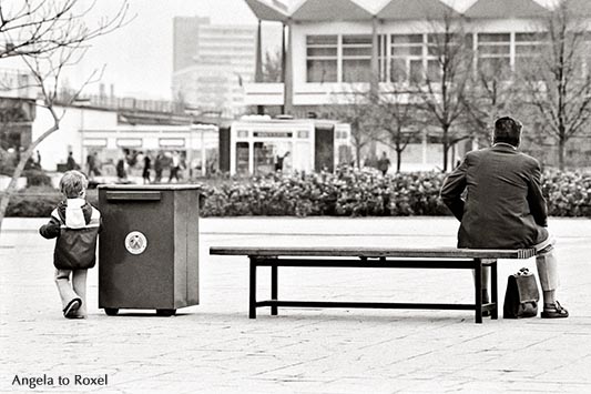 Mann sitzt auf einer Bank im Stadtzentrum, Aktentasche zwischen den Beinen, ein Junge links von ihm, Rückansicht, schwarzweiß, analog - Ostberlin 1981