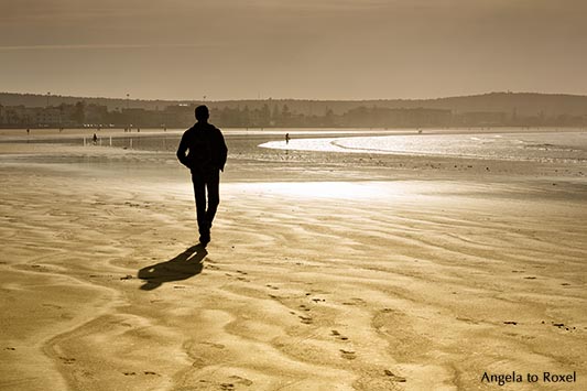 Man walking on Plage Tagharte in winter, backlight, early morning light - Essaouira, Morocco