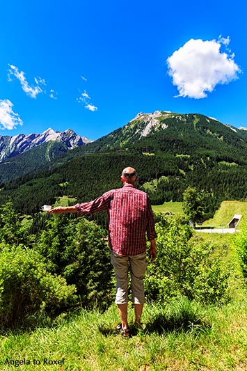 Mann hält eine Kaffeetasse in der Hand und schaut auf die Berge im Hintergrund, Rückenansicht - Graubünden