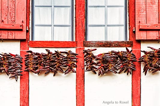 Chili-Schoten, aufgereiht auf langen Schnüren zum Trocknen, leuchtend rot vor einer weiß gekalkten Hauswand im Baskenland, Espelette - Frankreich 2012