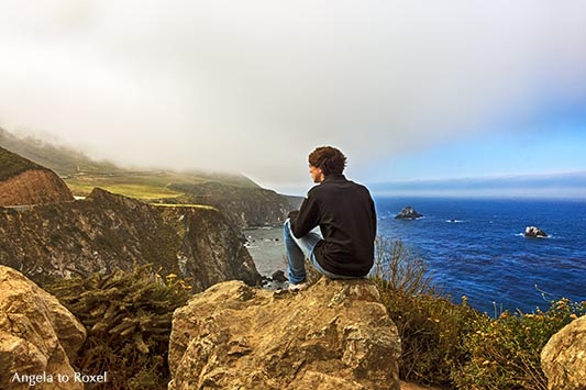 Junger Mann in Big Sur, sitzt auf einem Felsen an der Pazifikküste und schaut auf die Berge der Santa Lucia Range, Highway No 1 - Kalifornien 2011