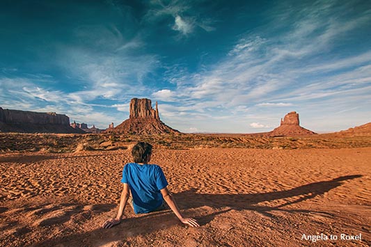 Junger Mann sitzt abends im Monument Valley und schaut zu den Butten, Rückenansicht, langer Schatten - Utah 2011