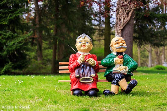 Fotografie: Comes a time - Zwei Gartenfiiguren, Oma und Opa sitzen nebeneinander auf einer Bank im Park, sie strickt, er liest - Bad Pyrmont 2013