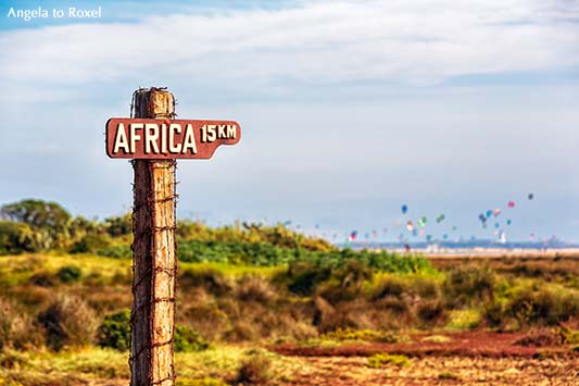 Wegweiser in Tarifa: 15 km bis Afrika - Schild am Campingplatz Rio Jara, im Hintergrund der Strand und die Kitesurfer von Tarifa, Cádiz, Spanien